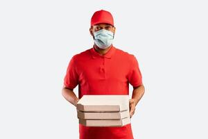 Pizza Delivery Concept. African Man Delivering Pizza Boxes From Pizzeria Restaurant To Home Door Wearing Mask Over Yellow Studio Background. photo