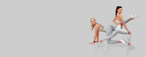 Two fitness enthusiasts showcase dynamic stretches wearing matching workout attire in a bright studio. photo