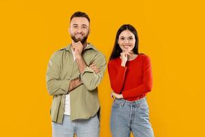A young couple stands side by side in a vibrant yellow setting. They share playful expressions while resting their chins on their hands, showcasing their affection and joy. photo