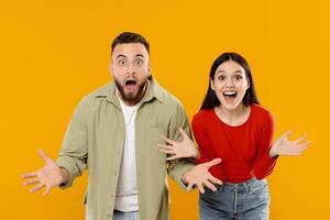 A joyful couple stands against a bright yellow background, both with wide smiles and surprised expressions. They are excited and share a moment of happiness and connection. photo