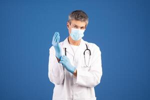 European doctor wearing a medical mask and gloves is getting ready to provide care. He is focused and ready for patient interaction in a clean, isolated environment. photo