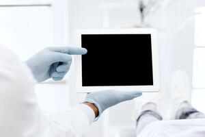 Black Dentist Showing Digital Tablet With Blank Screen To Female Patient During Check Up In Modern Stomatological Clinic, Demonstrating Dental Treatment Result Or Teeth X-Ray On Modern Gadget, Mockup photo