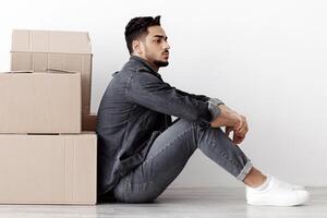 Upset arab family sitting separated by boxes on floor in empty apartment, having problem with relocating, white wall background, side view, copy space. Depressed middle-eastern couple at new home photo