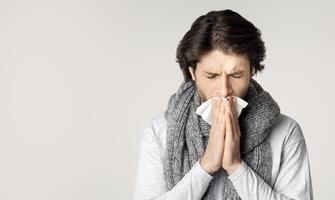 Guy with scarf around his neck, feels sick, sneezes in napkin photo