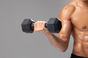 A young Brazilian man with an athletic build engages in strength training by lifting a dumbbell. He is focused on maintaining a healthy lifestyle while exercising indoors against a plain background. photo