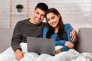 Stay At Home Concept. Self isolated spouses hugging and watching movie on laptop sitting on sofa, copy space photo