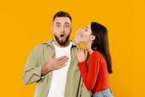 A young couple expresses affection as the woman whispers a secret to the man, who looks surprised. Their playful interaction captures the joy of intimacy in a vibrant, colorful setting. photo