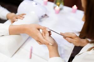 In a chic salon setting, a skilled technician carefully files a client's nails while they enjoy a pampering manicure. Soft candles provide a calming ambiance in the background. photo