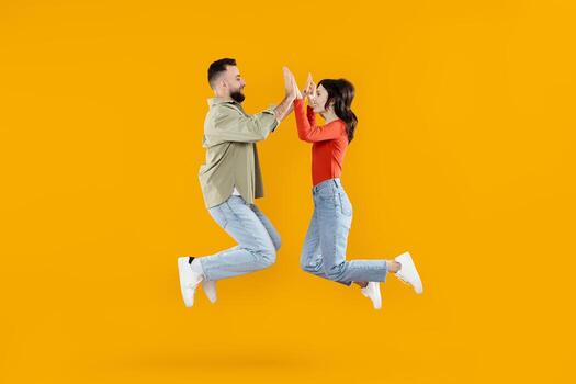A joyful couple leaps together in mid-air, expressing their affection and connection. They are dressed casually, creating a lively and vibrant atmosphere with a bright yellow background. photo