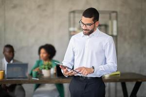 A group of professionals engage in a productive meeting in a contemporary office space. One member uses a tablet while others discuss, showcasing teamwork and collaboration. photo