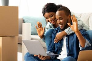 Happy African American Couple Making Call With Family Or Friends After Moving To Their Own Apartment, Cheerful Black Spouses Using Laptop Computer, Waving Hands At Web Camera And Smiling photo