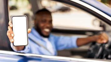 Closeup of black male driver holding smartphone with blank screen in hand, mock up, guy showing cell phone with white empty display, using mobile app for navigation, free copy space, selective focus photo