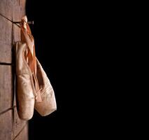 Used ballet shoes hanging on wooden background photo
