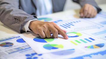 A person in a suit is pointing at graphs on a table photo