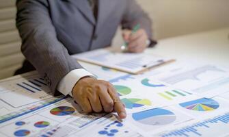 A man in a suit is pointing at graphs on a table photo