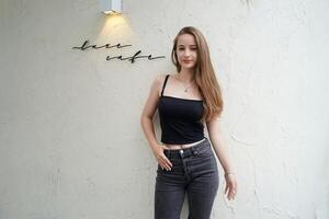 A woman in jeans and a black top standing in front of a wall photo