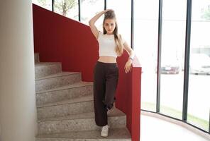 A woman in a white top and brown pants standing on a stairway photo