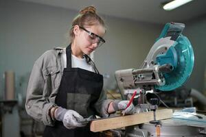 A woman in a black apron is using a circular saw photo