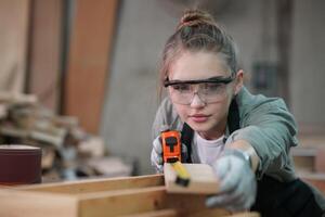 A woman in glasses is working on a piece of wood photo