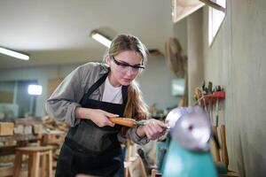 A woman in a black apron is working on a piece of wood photo