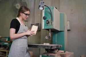A woman in an apron is working on a piece of wood photo