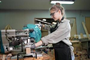 A woman in an apron is using a circular saw photo