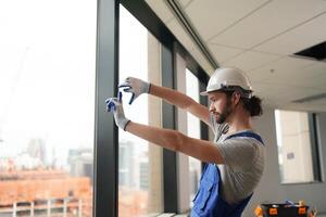 A man in a hard hat and overalls is fixing a window photo