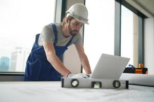 A man in overalls working on a laptop photo