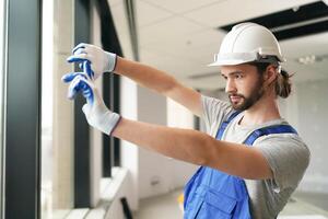 A man in a hard hat and overalls is cleaning a window photo