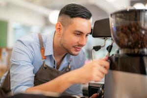 A man in an apron is using a coffee grinder photo