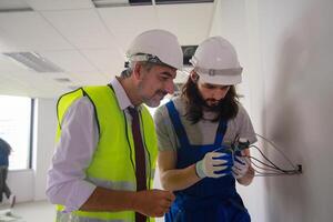 Two men in hard hats and safety vests working on electrical equipment photo