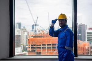 A man in a hard hat standing in front of a window with a city in the background photo