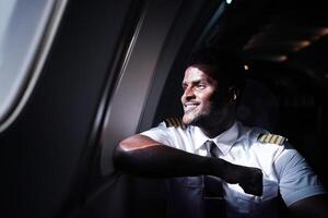 A man in a pilot uniform is smiling while sitting in an airplane photo