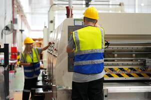 Two workers in safety vests and hard hats working on a machine photo