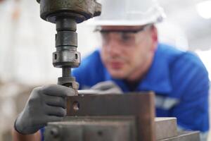 A man in a blue shirt and white helmet is working on a machine photo