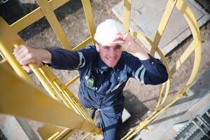 A man in a hard hat and overalls is standing on a ladder photo
