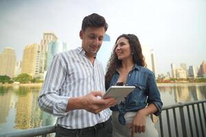 un hombre y mujer en pie siguiente a un río mirando a un tableta foto