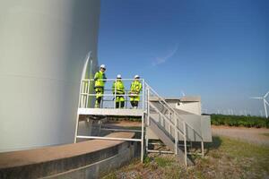 A group of people standing on a ladder next to a wind turbine photo
