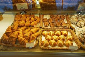 Baskets of plain butter, almond chocolate croissant, hot cross bun, ham and cheese Tiger claw, bacon and ham sandwiches, Kouign Amann and maple pull apart displayed in glass showcase box photo