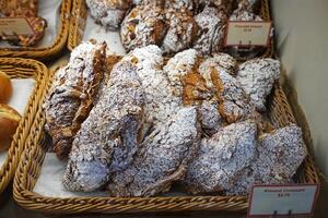 Baskets of plain butter, almond chocolate croissant, hot cross bun, ham and cheese Tiger claw, bacon and ham sandwiches, Kouign Amann and maple pull apart displayed in glass showcase box photo