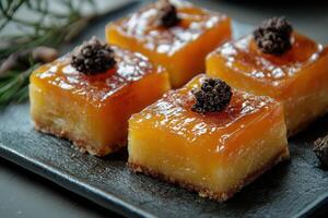 Four glossy orange squares of dessert on a dark grey plate. photo