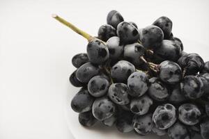 A branch of black grapes on a white plate. photo