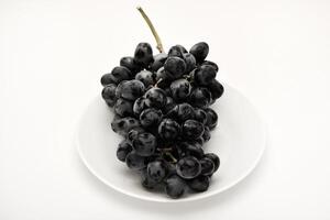 A branch of black grapes on a white plate. photo