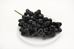 A branch of black grapes on a white plate. photo