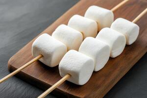 Fluffy marshmallows skewered on wooden sticks photo
