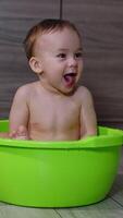 Happy lovely toddler being washed in the tub. Smiling kid sits in the washbowl showing tongue to camera. Vertical video