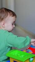 Caucasian baby playing with a toy on the floor. Calm kid presses on toy mouth but it pops up again. Christmas tree at backdrop. Vertical video