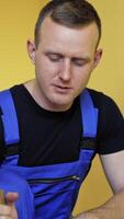 Portrait of a worker preparing dye for renovation. Craftsman in blue overalls mixing paint on the background of ladder in the room. Vertical video