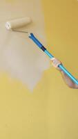 Room improvement with a new color. Professional worker in blue overalls painting wall with a paint roller on a long handle on. Craftsman working. Vertical video