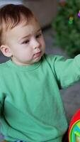 Cute child holds a part from toy surprised that it fell off. Adorable boy continues his game pressing buttons on a toy. Christmas tree. Vertical video